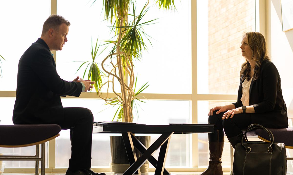 A man and woman sitting across from one another at a table in a lobby.