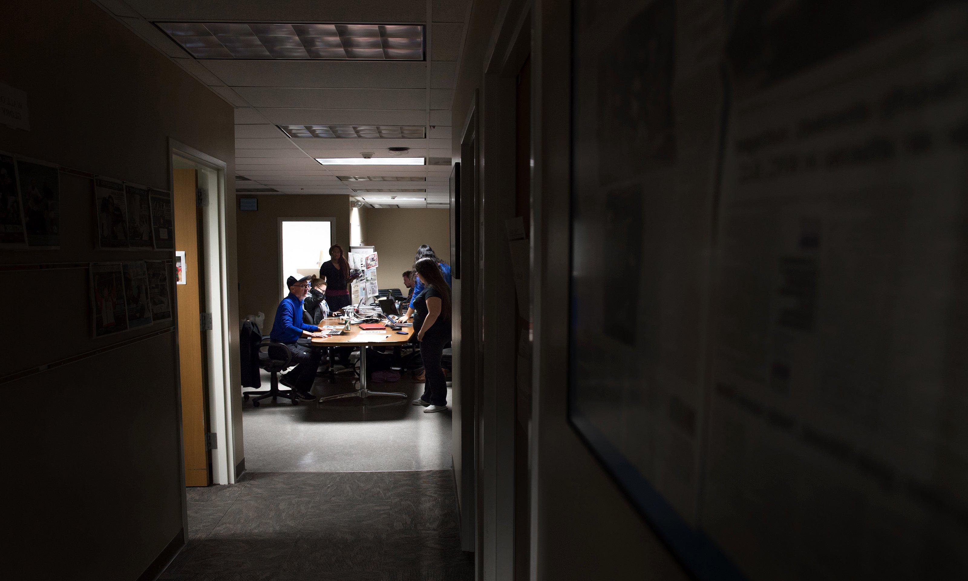 A dark hallway leading to an open space with a table and people