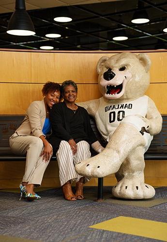 Two women sitting together next to bear mascot